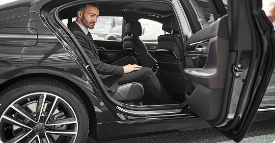 Professional man in a suit seated comfortably in the rear of a premium black sedan, illustrating space and executive comfort.