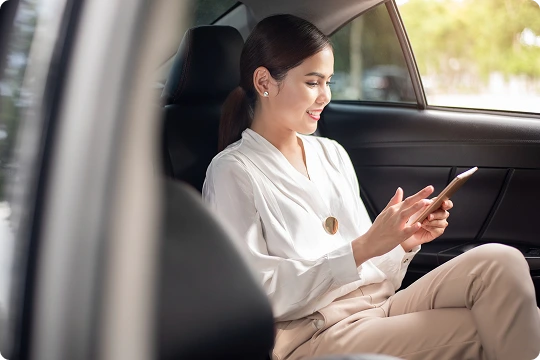 Smiling female passenger in a white blouse using her smartphone while riding in the backseat of a luxury vehicle