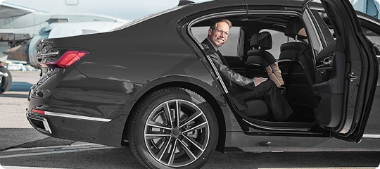 Business traveler smiling as he boards a luxury black sedan at the airport, highlighting professional and seamless executive airport transfers