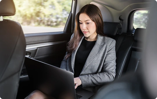 Focused businesswoman in a plaid blazer working on her laptop in the rear seat of a chauffeured SUV