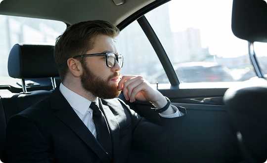 Bearded businessman in suit and sunglasses gazing out the window of a luxury vehicle, conveying comfort and privacy during travel.